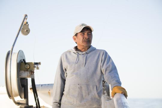 Man stands along the railing of a fishing vessel, next to a rig