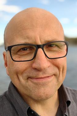 A man with glasses smiles at the camera.